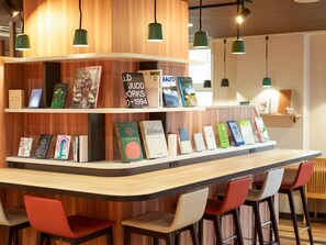 A modern bar area with wooden shelves displaying books, a curved counter, and red and white bar stools. - Comfort Hotel Kumamoto Shinshigai (Kumamoto)