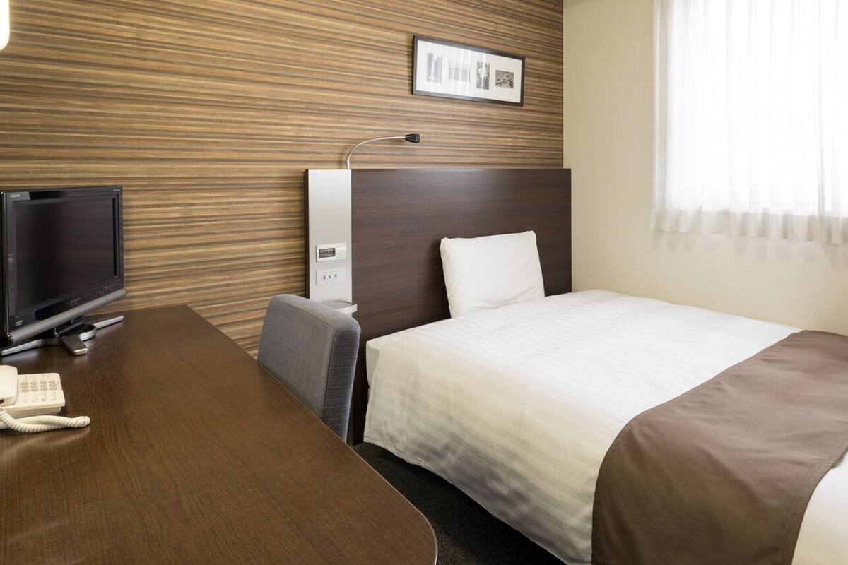 Habitación de hotel con cama, escritorio, teléfono, televisor y panel de control en la pared.