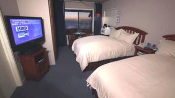 A hotel room with two beds, a television displaying HBO and Cinemascope logos, a desk with a lamp, and a view of the city through the window.