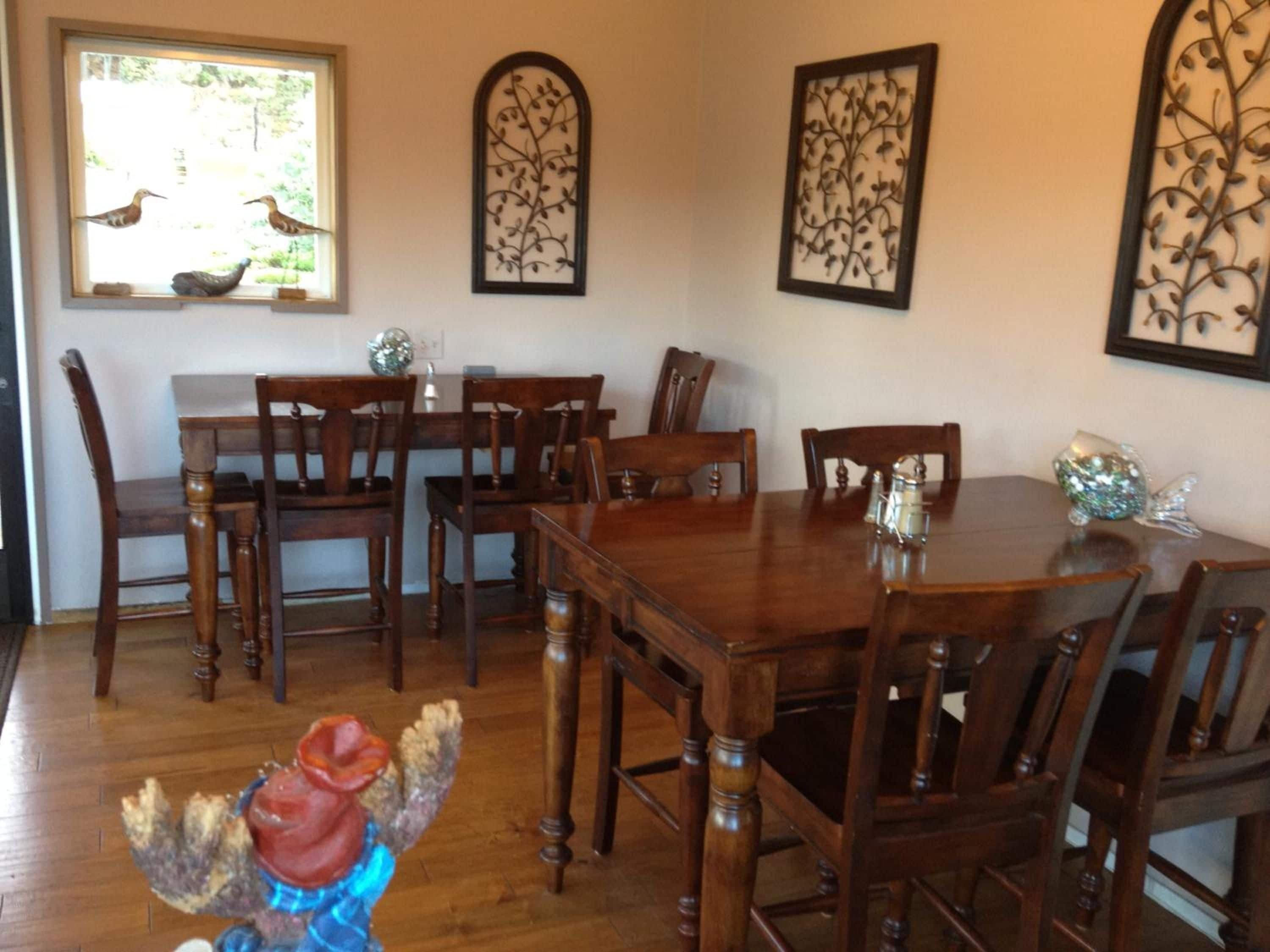 A dining room with a wooden table and chairs, decorative wall art, and a window with a view of birds.