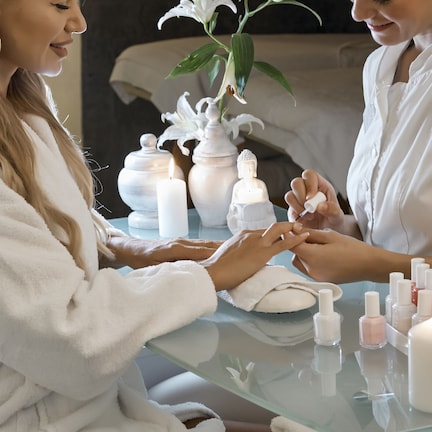 A person receiving a manicure in a spa setting with a glass table, candles, and a Buddha statue in the background.