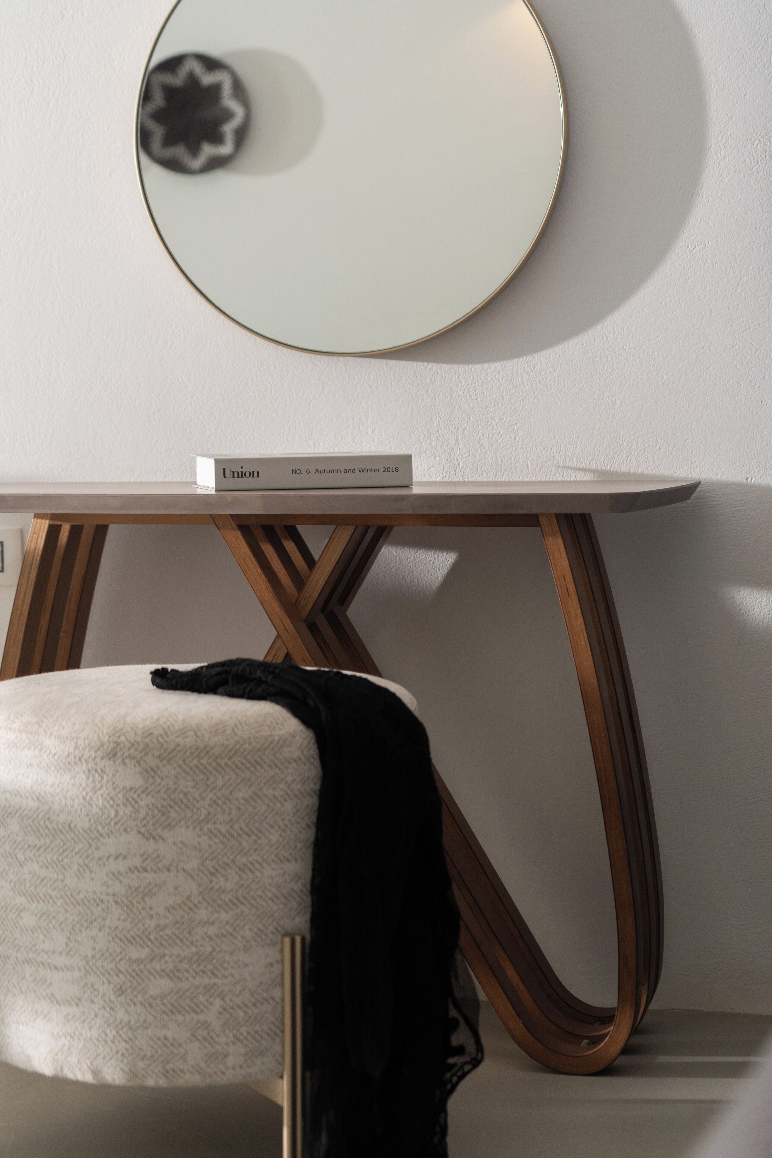 Une chambre moderne avec un grand miroir rond au mur, une chaise blanche agrémentée d’un coussin noir, et une table aux pieds en bois et au plateau blanc.