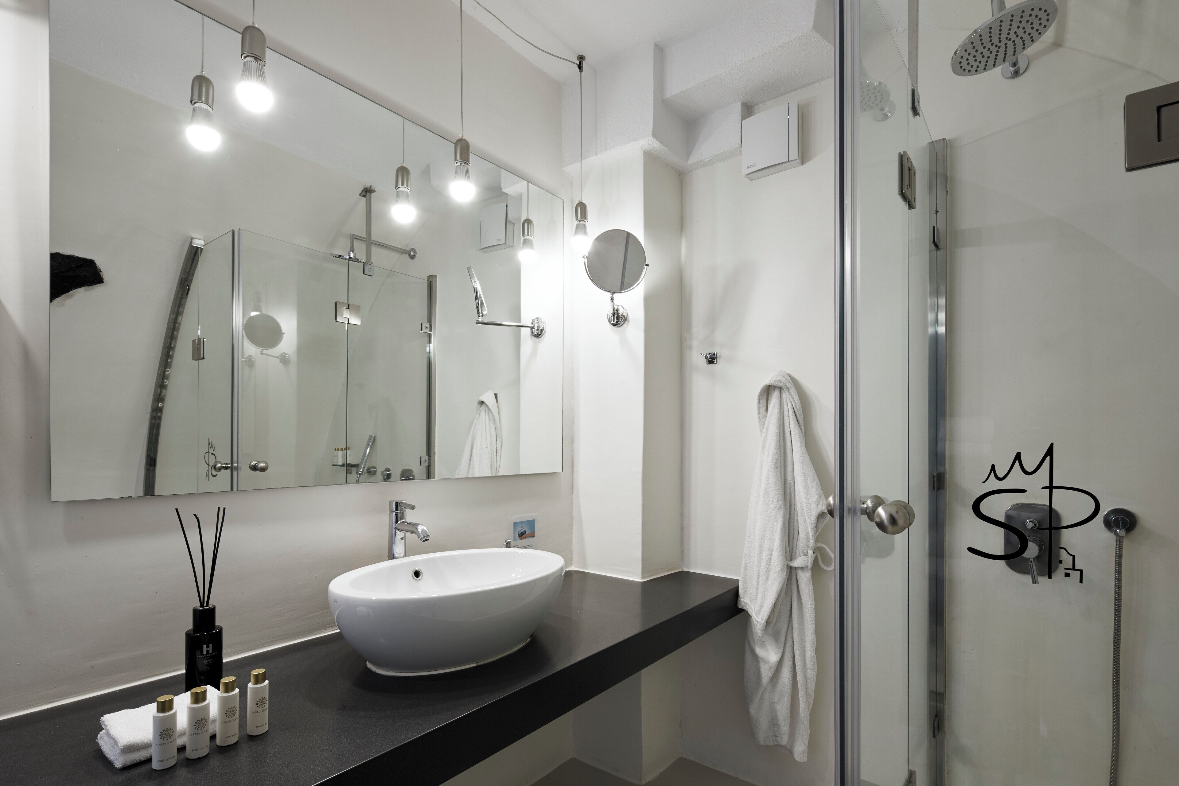 A modern bathroom with a large mirror, a round sink, and a glass shower enclosure.