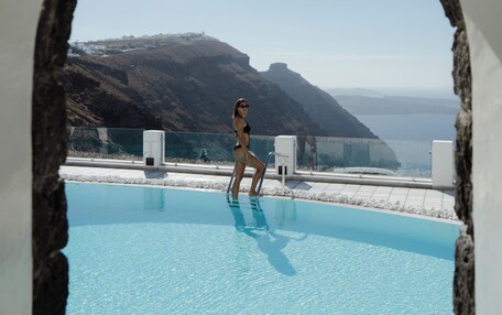 A woman in a bikini standing in a pool with a view of a mountainous landscape and a clear sky.