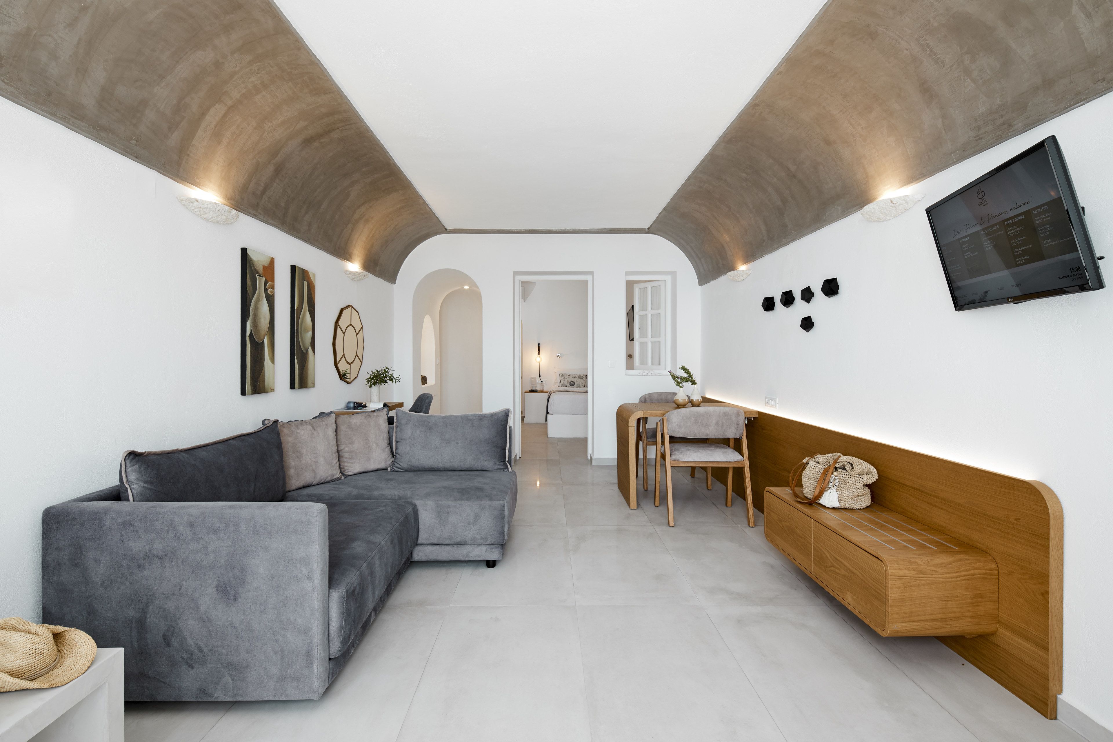 A modern living room with a grey sectional sofa, a wooden bench, and a TV mounted on the wall.