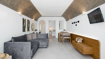 A modern living room with a grey sectional sofa, a wooden bench, and a TV mounted on the wall.