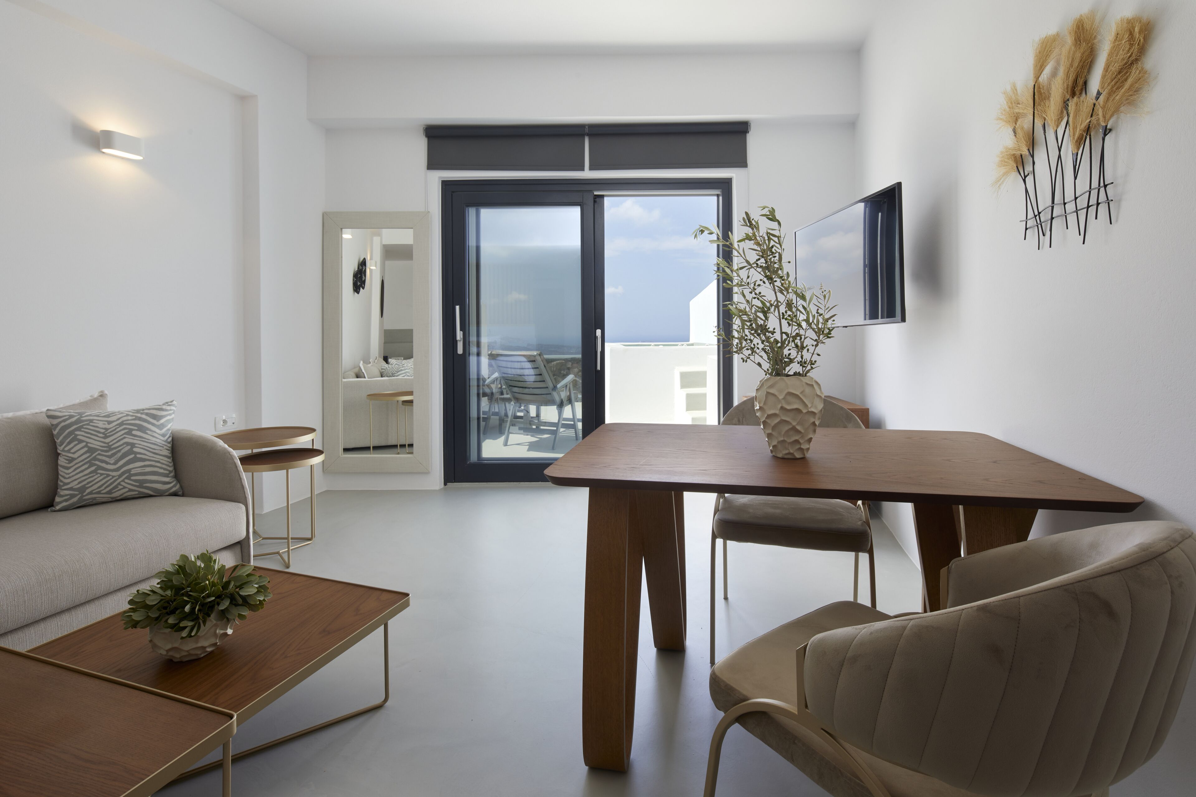 A modern living room with a sofa, coffee table, and dining table. There is a balcony with a view of the sea.