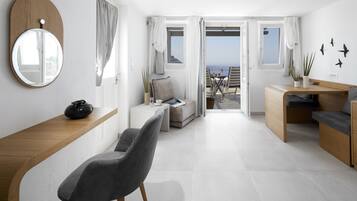 Una stanza moderna e luminosa, con una scrivania in legno, una sedia grigia, un piccolo divano e vista sul mare attraverso porte aperte.
