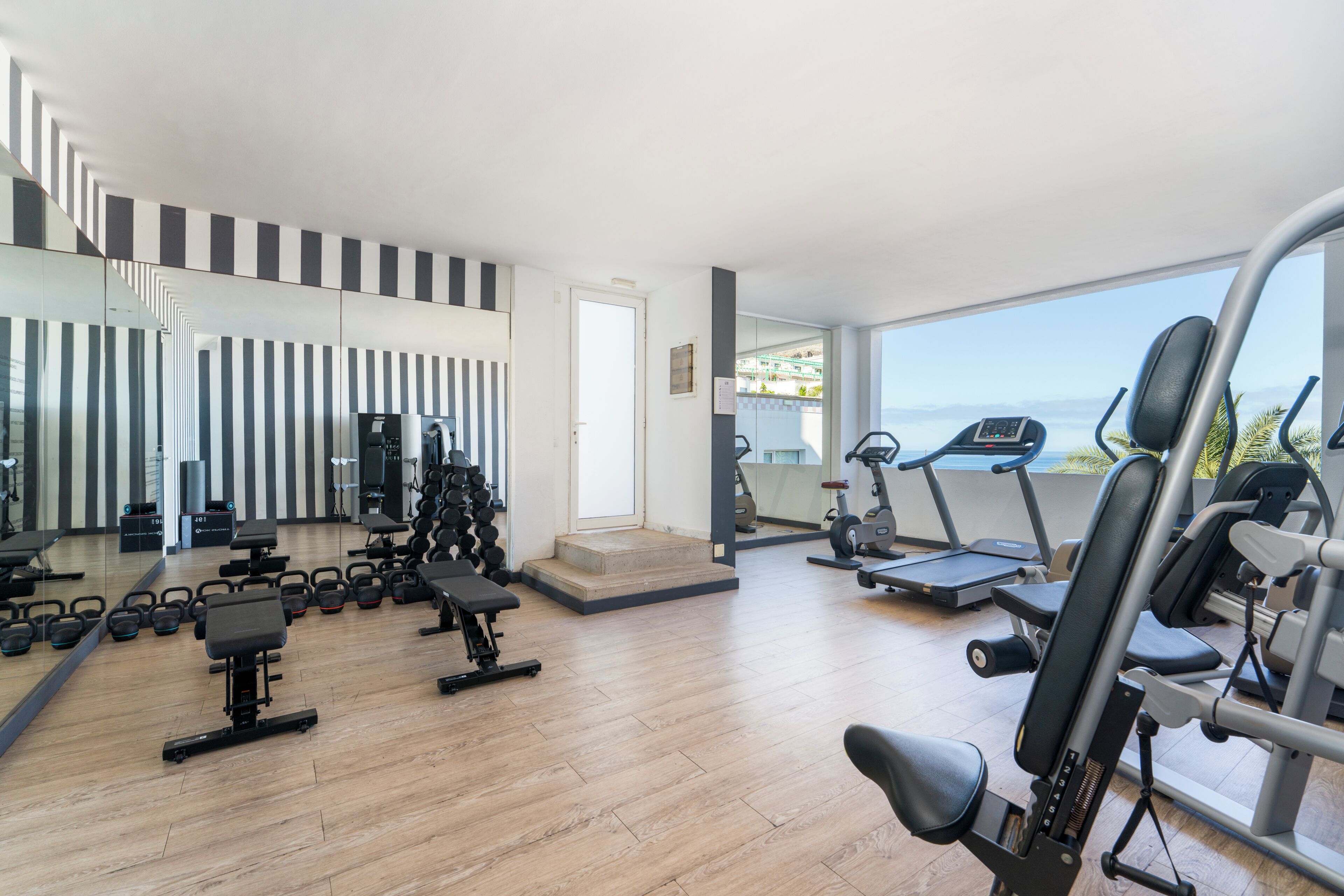 A gym with exercise equipment, a mirror, and a view of the sea.