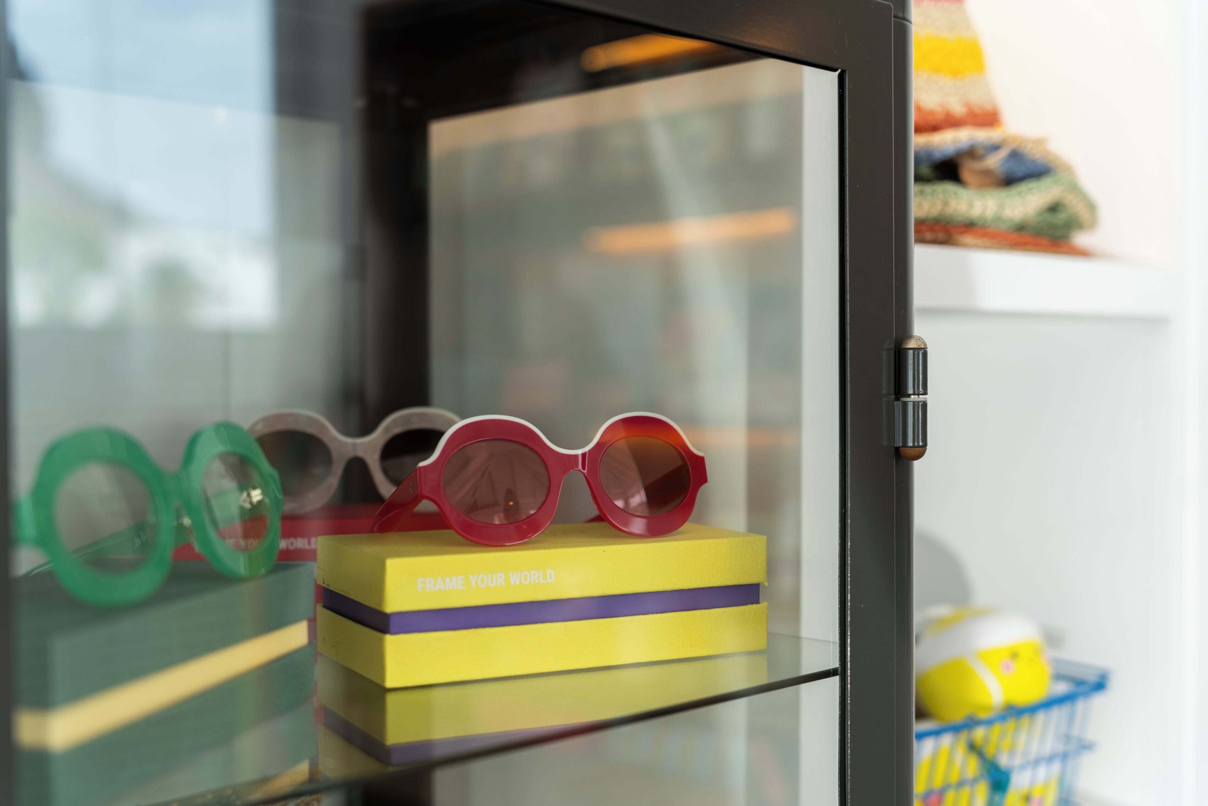 A display case with a pair of glasses on a yellow box labeled 'FRAME YOUR WORLD'.