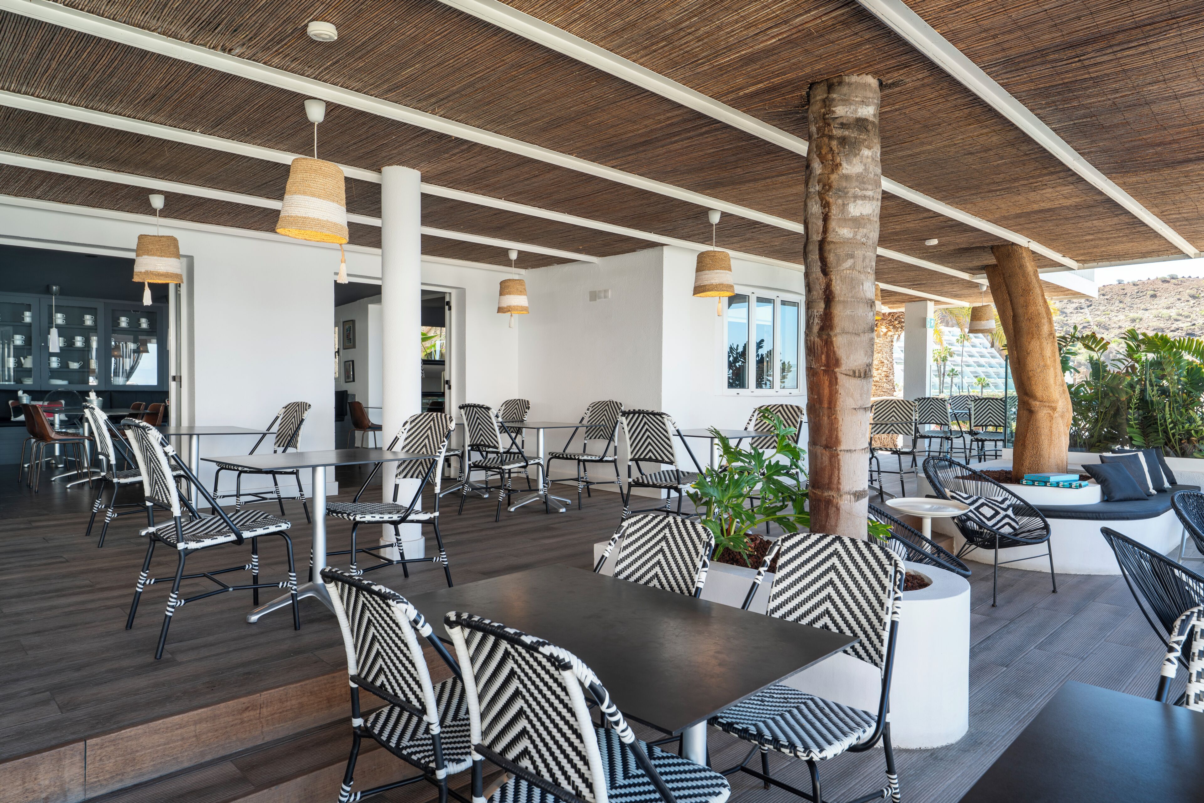 Un espace de restauration en plein air avec des chaises à rayures noires et blanches, une table centrale et des lampes suspendues.