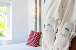A white bathrobe with a towel and slippers, a red patterned pillow, and a window with greenery outside. - Marina Bayview - Adults Only (Mogan)