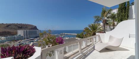 A balcony with a view of the sea, a white building, and some plants.