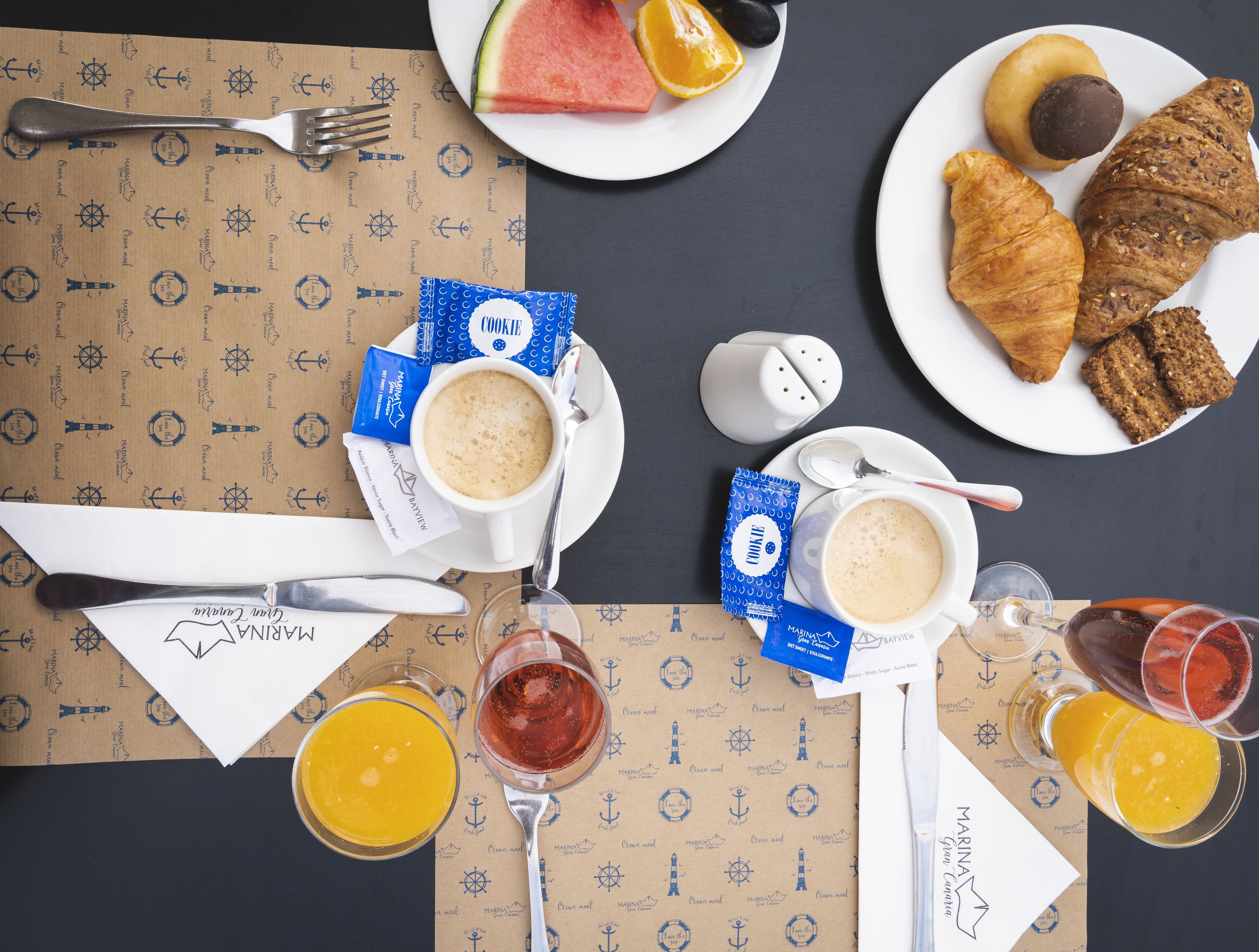 A breakfast setting with coffee, croissants, and fruit on plates, along with a salt shaker and a menu.