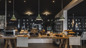 A modern kitchen with wooden tables, hanging green pendant lights, and shelves stocked with kitchenware.