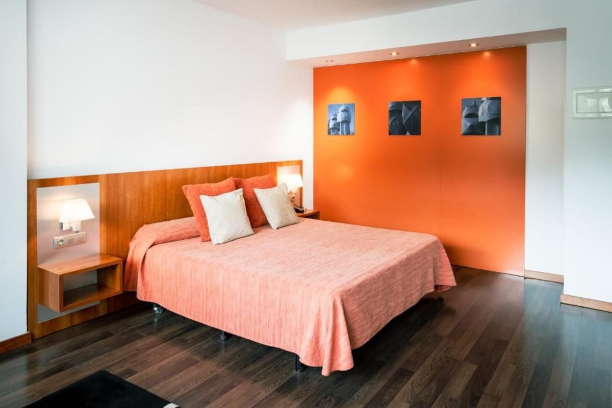 Ein modernes Schlafzimmer mit einem großen Bett, einem Holz-Kopfteil und einer orangefarbenen Wand mit gerahmten Bildern.