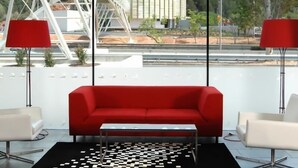 Une pièce moderne avec un canapé rouge, une petite table et deux chaises blanches. Un tapis noir et blanc à motifs recouvre le sol.