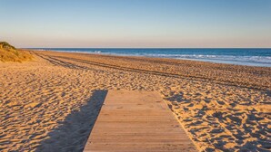 Une promenade en bois mène à une plage de sable et de galets, avec l’océan en arrière-plan.