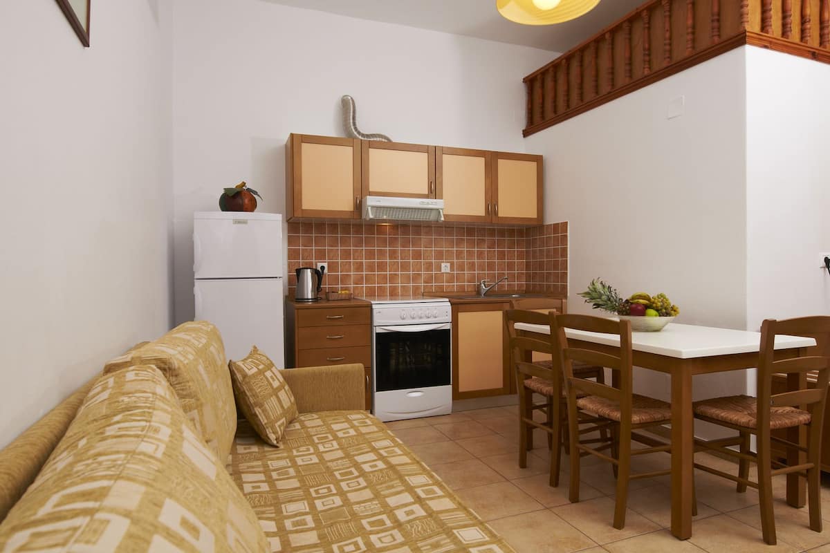 Uma cozinha compacta com geladeira, fogão e pia. Há uma mesa de jantar com cadeiras e um sofá na sala de estar.