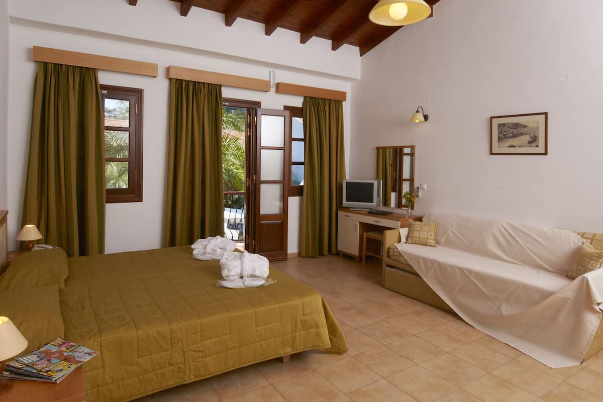 Quarto de hotel com cama, escrivaninha, televisão e sofá.