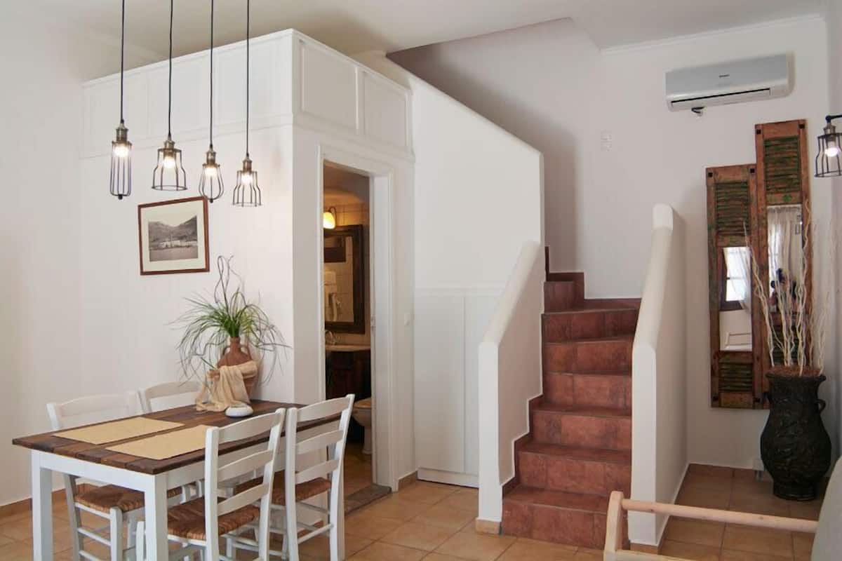 Uma área de refeições com uma mesa, cadeiras, uma escada e um vaso de planta.