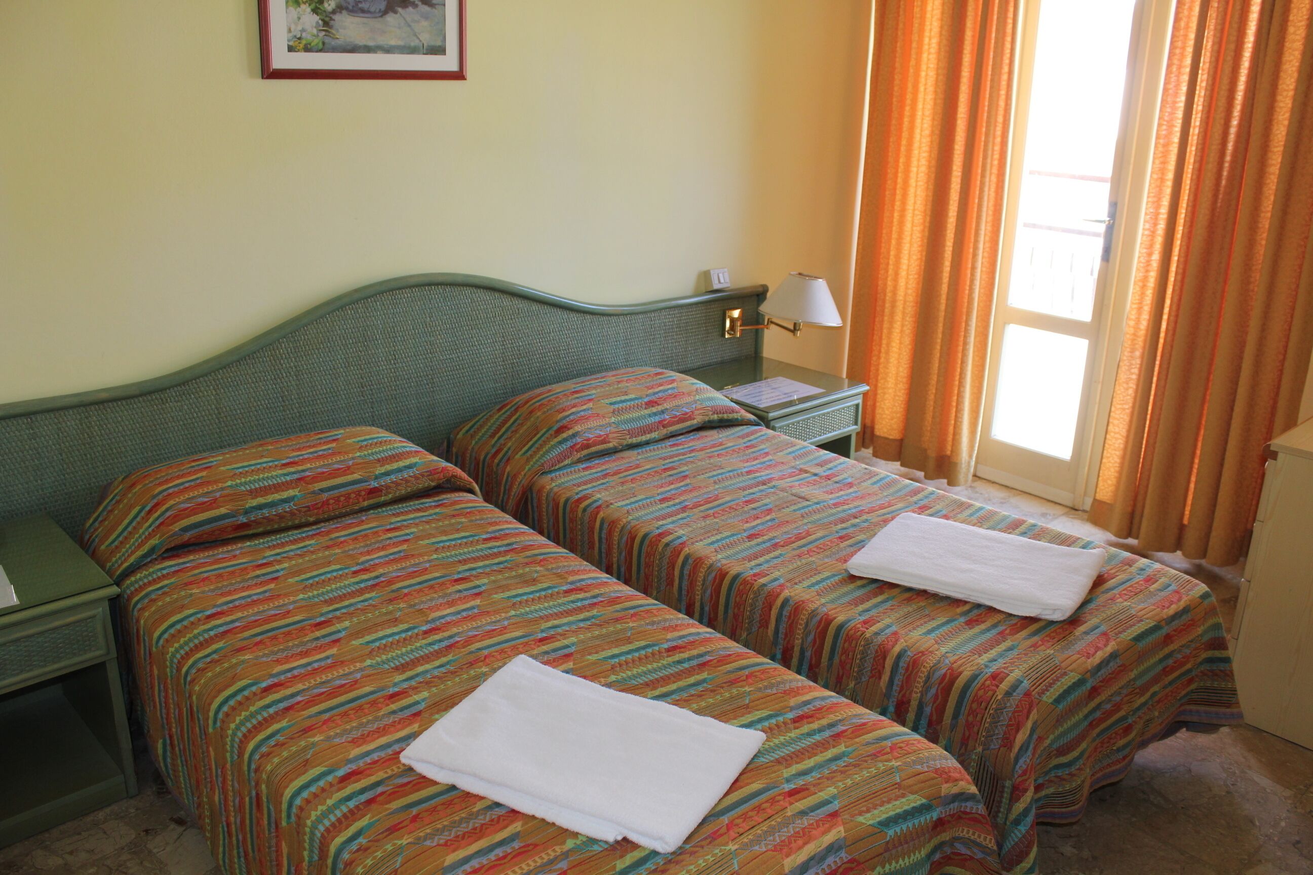 A room with two beds, a nightstand, a lamp, and a window with curtains.