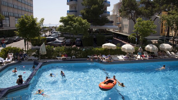 Ein Poolbereich mit mehreren Pools, Liegestühlen, Sonnenschirmen und einem hoch aufragenden Gebäude im Hintergrund.
