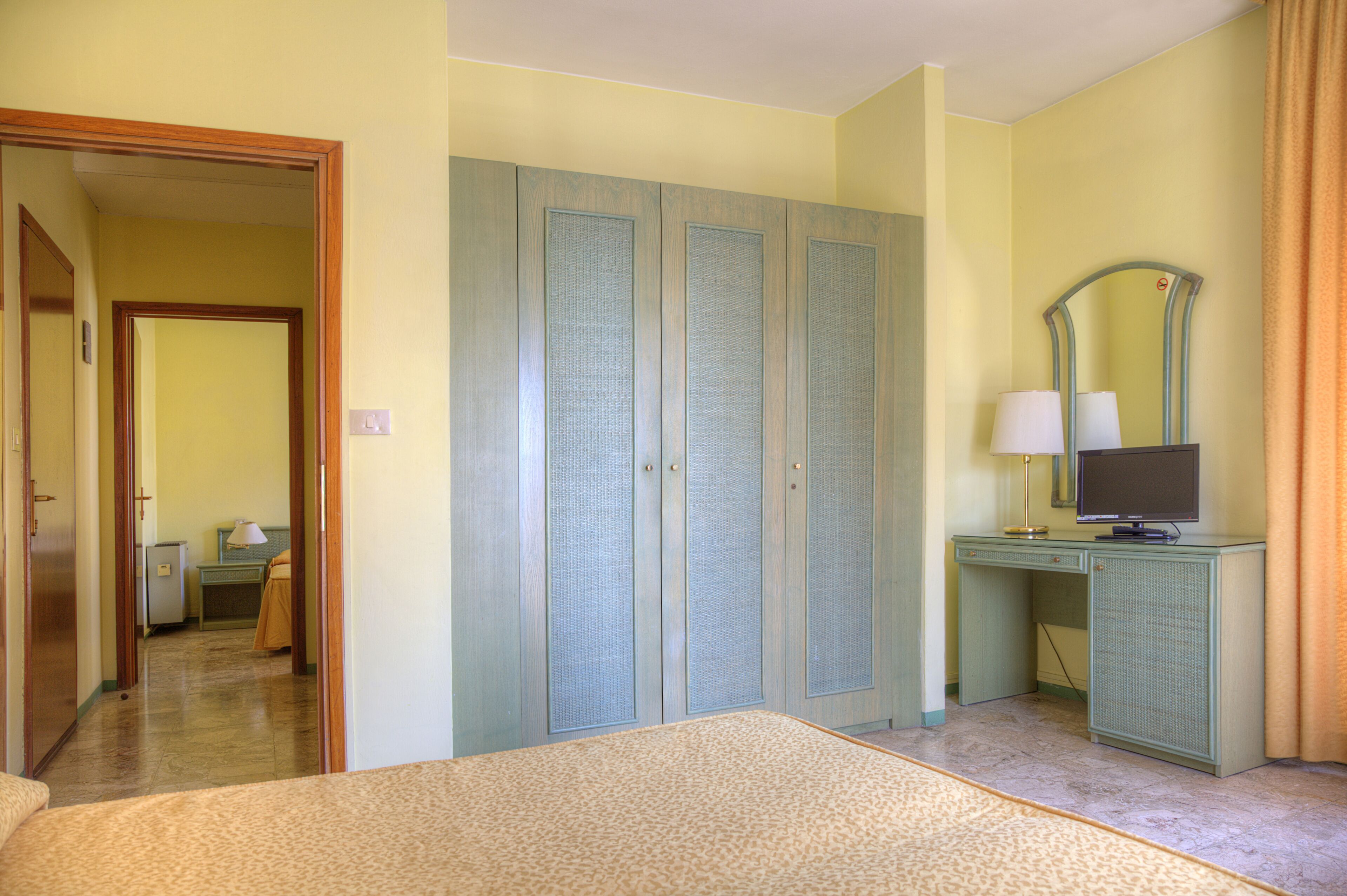 Una habitación de hotel con cama, escritorio con computadora, armario y espejo.