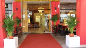 Eine Hotelhalle mit rotem Teppich, Zimmerpflanzen, einem Chandelier und einer Rezeption.