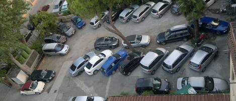 An aerial view of a parking lot with multiple cars parked in rows, surrounded by trees and buildings.