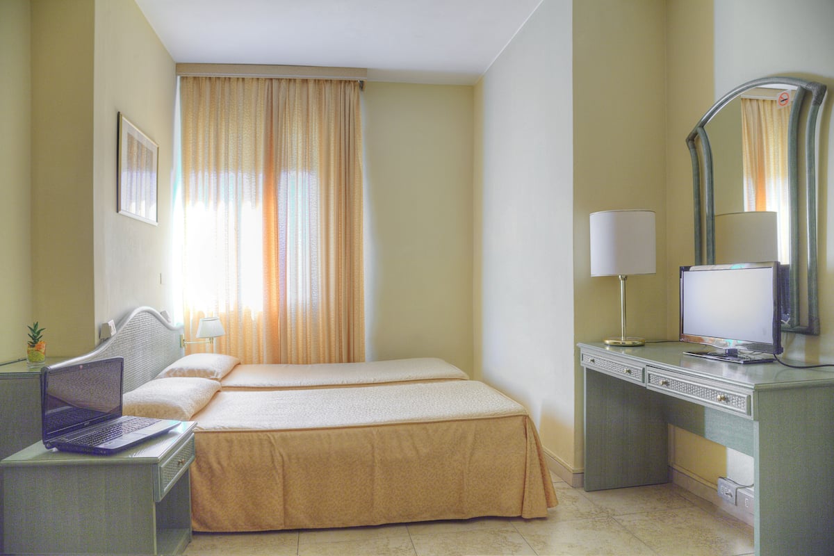 A hotel room with two beds, a desk with a laptop, a desk lamp, and a large mirror.