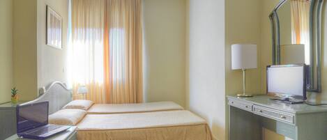 Habitación de hotel con dos camas, un escritorio con una computadora portátil, una lámpara de escritorio y un espejo grande.