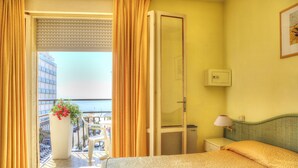 Ein Hotelzimmer mit Bett, Nachttisch, Lampe und Meerblick durch eine Balkontür.