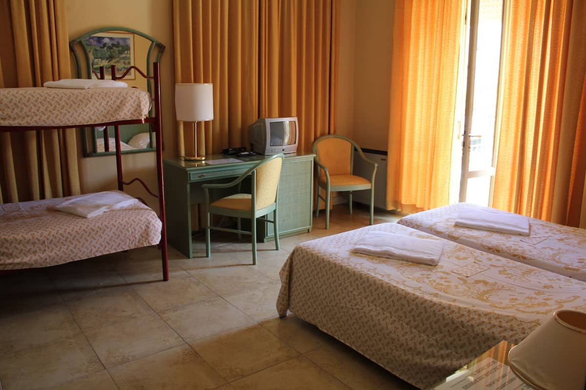 A hotel room with two single beds, a desk with a computer, a chair, and a television.