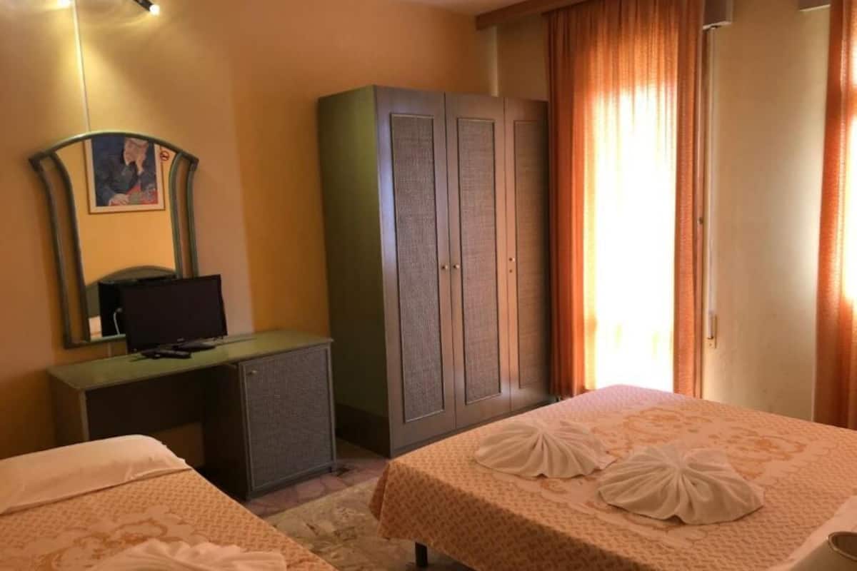 A hotel room with two beds, a desk with a computer, a wardrobe, and a painting on the wall.