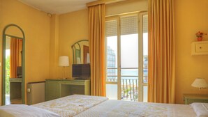 Ein Hotelzimmer mit Bett, Fernseher auf einem Schreibtisch, einem Balkon mit Vorhängen und Blick aufs Meer.