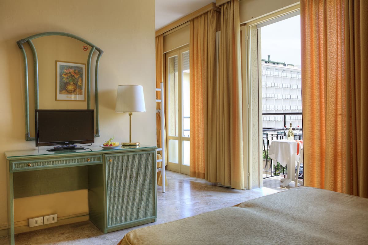 A hotel room with a bed, a desk with a television, a lamp, and a view of the outside balcony.