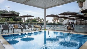 Una piscina con sillas de descanso y sombrillas, rodeada de vegetación y un cielo despejado.