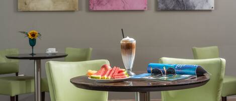Un comedor con una mesa dispuesta para dos personas, que incluye una bebida postre, rebanadas de sandía y una revista.