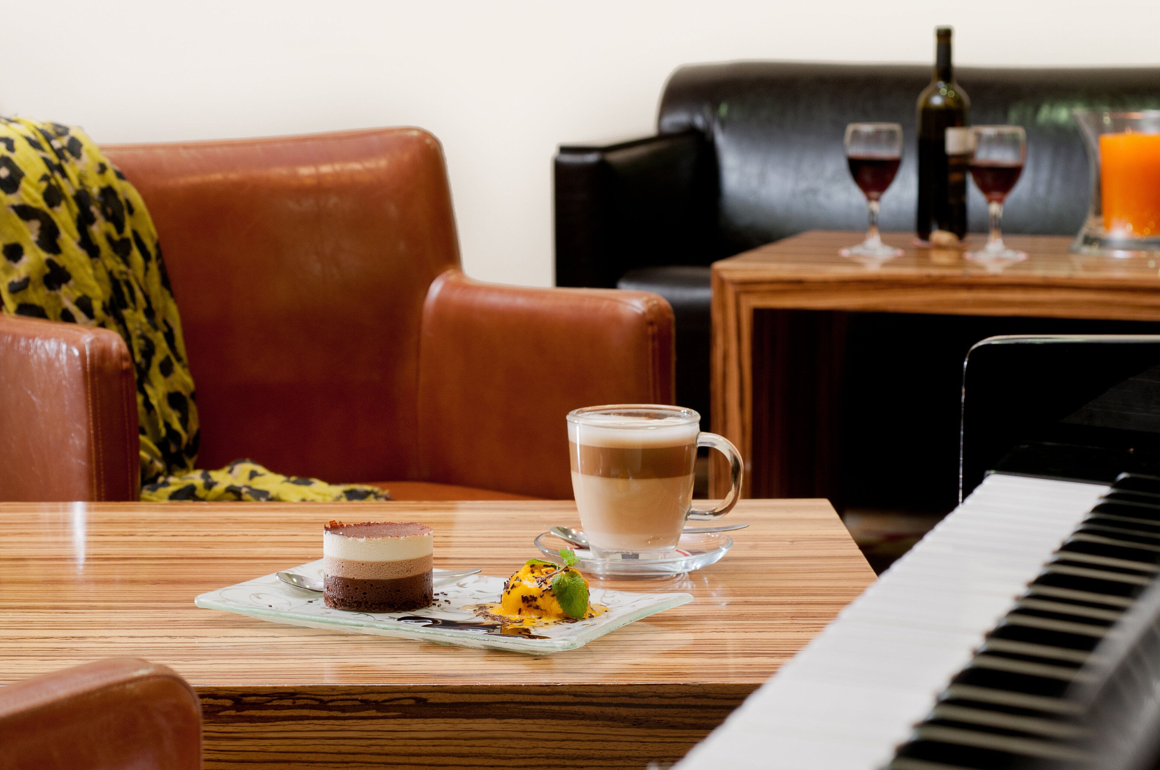 A dining table with a dessert plate, a cup of coffee, and a piano in the foreground.