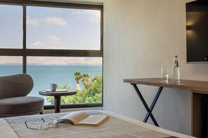 Une chambre d’hôtel avec une grande fenêtre, un lit, une petite table avec des verres et un livre, et un téléviseur fixé au mur.