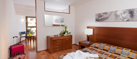 Habitación de hotel con cama, cómoda, escritorio, silla, maleta y ventana.