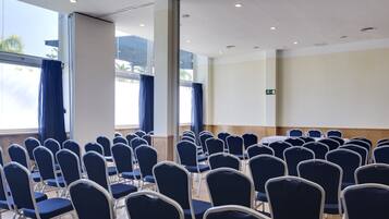 A conference room with rows of chairs, large windows with curtains, and a whiteboard.