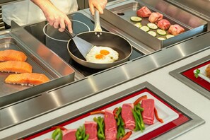 A kitchen with a griddle, a pan with eggs, and various meats and vegetables on display.