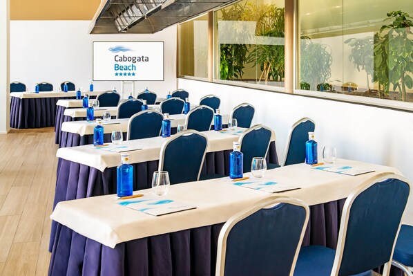 Un salón de conferencias con mesas dispuestas para reuniones, con sillas azules y botellas de agua.