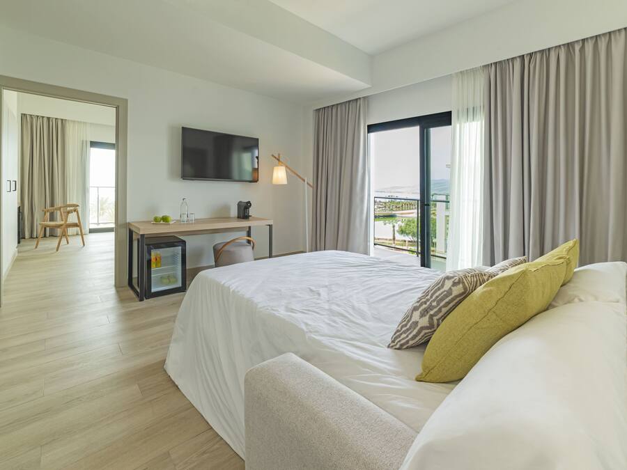 Una habitación de hotel moderna con una cama grande, un escritorio con una silla, un televisor y un balcón con cortinas.
