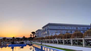 Un hotel con piscina, palmeras y un atardecer de fondo.