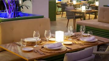 A dining area with tables set for two, featuring woven placemats, white napkins, and clear glassware.