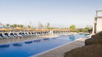 A pool area with lounge chairs and umbrellas, surrounded by palm trees and a clear sky.
