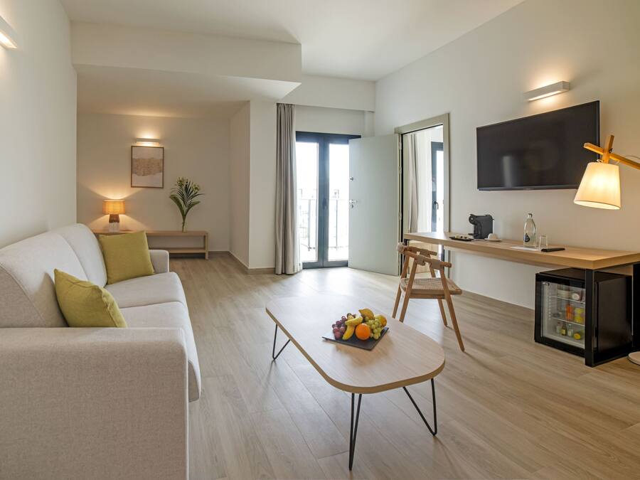 A modern living room with a sofa, a coffee table with fruit, a TV, and a small refrigerator.